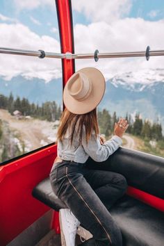 a woman sitting on the back of a red bus looking out at mountains and trees