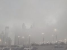 cars are parked in a parking lot on a foggy day with buildings in the background