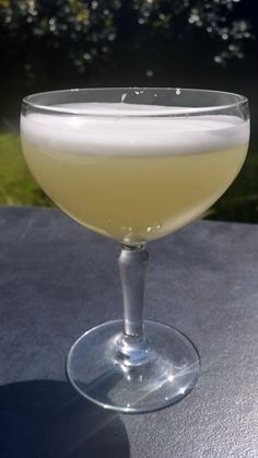 a glass filled with liquid sitting on top of a table next to a tree in the background