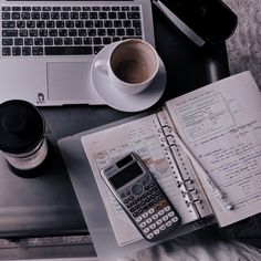 an open notebook, calculator and coffee on a desk