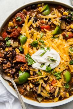 a white bowl filled with chili, beans, cheese and tortilla bread topped with sour cream