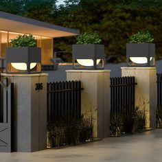 three planters with plants on top of them are lit up in front of a house