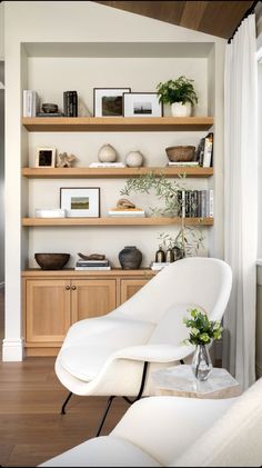 a white chair sitting in front of a wooden shelf filled with books and vases