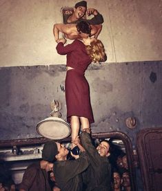 two people standing on top of each other in front of a man hanging upside down