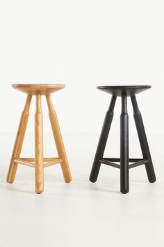 two wooden stools sitting next to each other on a white surface, one black and the other wood