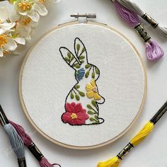 an embroidered bunny with flowers and tassels next to some embroiderying tools on a white surface