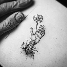 a hand holding a flower on top of a piece of paper next to a glove