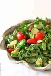 a salad with tomatoes, avocado and spinach in a bowl on a table