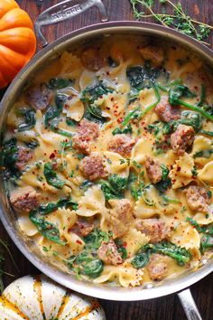 a skillet filled with pasta and spinach next to pumpkins on the table