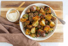 a white bowl filled with potatoes next to a wooden cutting board