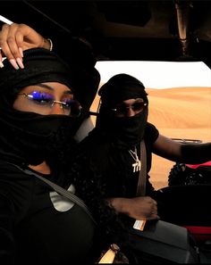 two women in black headscarves and sunglasses are sitting in a vehicle on the desert