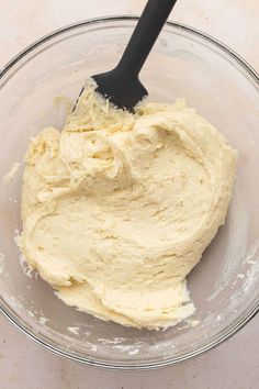 a glass bowl filled with batter and a black plastic spoon in the middle of it