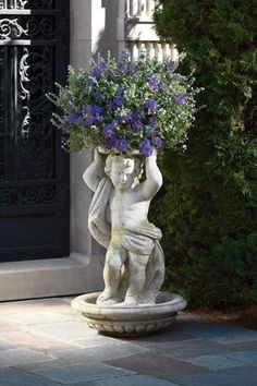 a statue holding a potted plant with purple flowers in it's hands on a patio