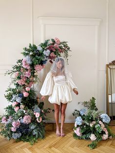 a woman in a wedding dress standing next to a floral arch with flowers on it