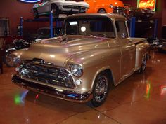 an old truck is parked in a garage with other classic cars on display behind it