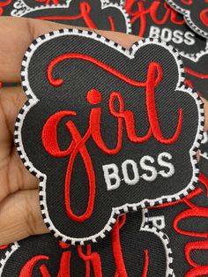 a hand holding a black and red patch with the word girl boss on it