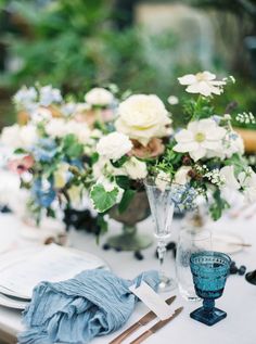 the table is set with white and blue flowers in vases, napkins, and glasses