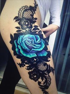 a woman's thigh with a blue rose tattoo on the side and black lace around it