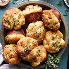 baked breads with herbs in a bowl on top of a blue tablecloth next to utensils