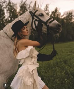 a woman in a white dress and black hat standing next to a horse