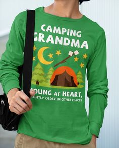 a woman wearing a green camping grandma t - shirt holding a black bag and looking at the camera