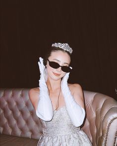 a woman wearing white gloves and a tiara sitting on a pink couch with her hands to her face