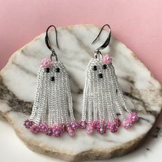 the earrings are decorated with pink and white beaded fringes on top of a marble slab