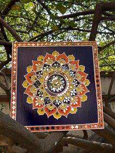 a painting hanging from a tree in front of a building with lots of leaves on it