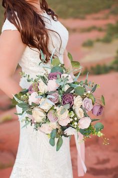 a woman in a wedding dress holding a bridal bouquet with purple and white flowers