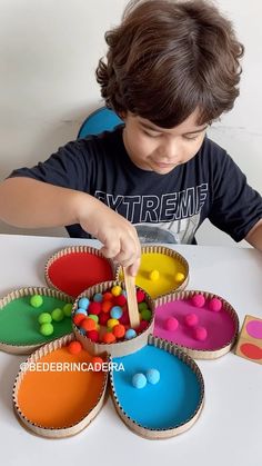 a young boy is playing with colored paper cups and spoons in the shape of flowers