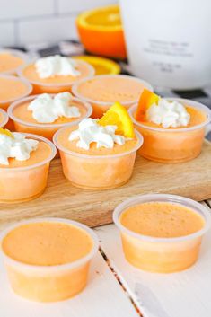 small cups filled with orange jello sitting on top of a wooden tray next to an orange slice