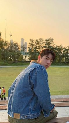 a man sitting on top of a wooden bench next to a park filled with people