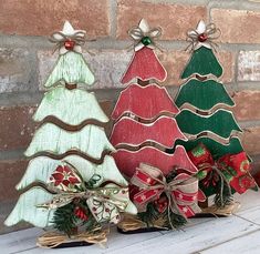 three wooden christmas trees sitting next to each other on a white table with red and green bows