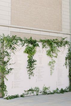 an outdoor wedding ceremony with greenery on the wall and seating chart in front of it