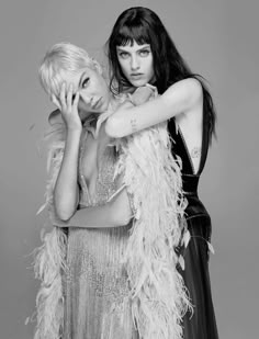 two women dressed in black and white posing for the camera with feathers around their necks