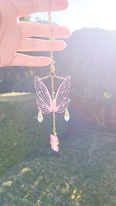 a person holding onto a pink butterfly necklace in their hand with the sun shining behind them