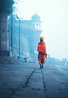 a person in an orange outfit walking down the street on a foggy, dreary day