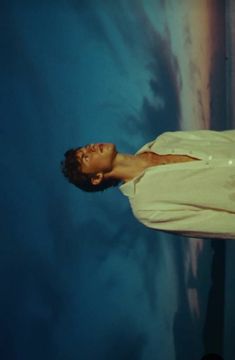 a man standing in front of a blue sky with clouds on the wall behind him