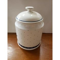 a white ceramic jar with black dots on the bottom and blue trim around the lid