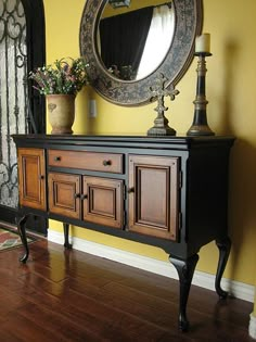 a black and brown dresser sitting next to a mirror on top of a wooden floor