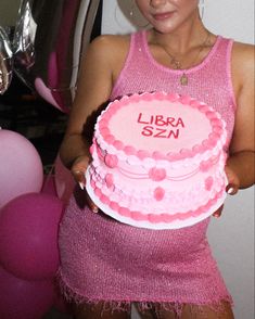 a woman holding a pink birthday cake in her hands