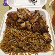 a plastic container filled with noodles and meat on top of a table next to a fork