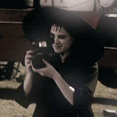 a woman holding a camera up to her face in front of an old train car