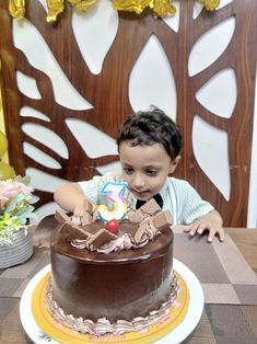 a young boy sitting at a table in front of a chocolate cake with the number five on it