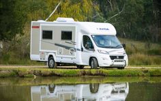 an rv parked next to a body of water with trees in the backgroud