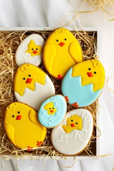 four decorated cookies in a box with straw on the floor next to it and eggs