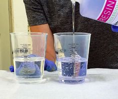 a person pouring water into two glasses on top of a white table with blue gloves