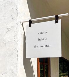 a white sign hanging from the side of a building that says sunrise behind the mountain