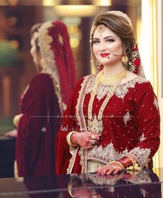 a woman in a red bridal outfit standing next to a mirror with her hands on her hips