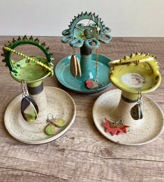 three ceramic dishes are sitting on a wooden table with beads and other items hanging from them